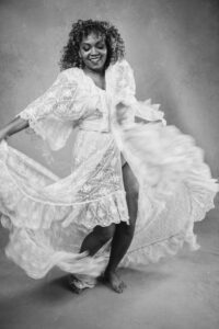 Black woman wearing a long white lace dress dancing to the camera