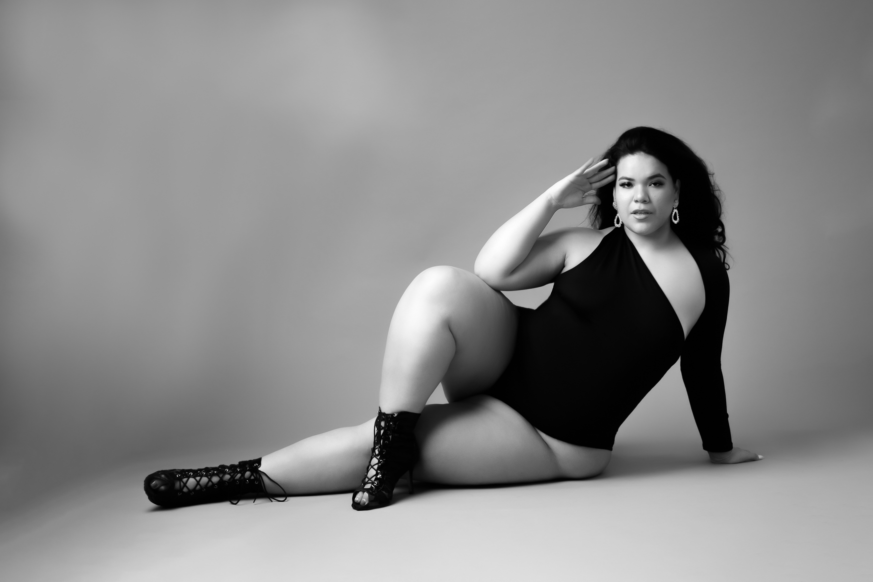 A woman sitting on the floor wearing black short boots and a black one piece body suit