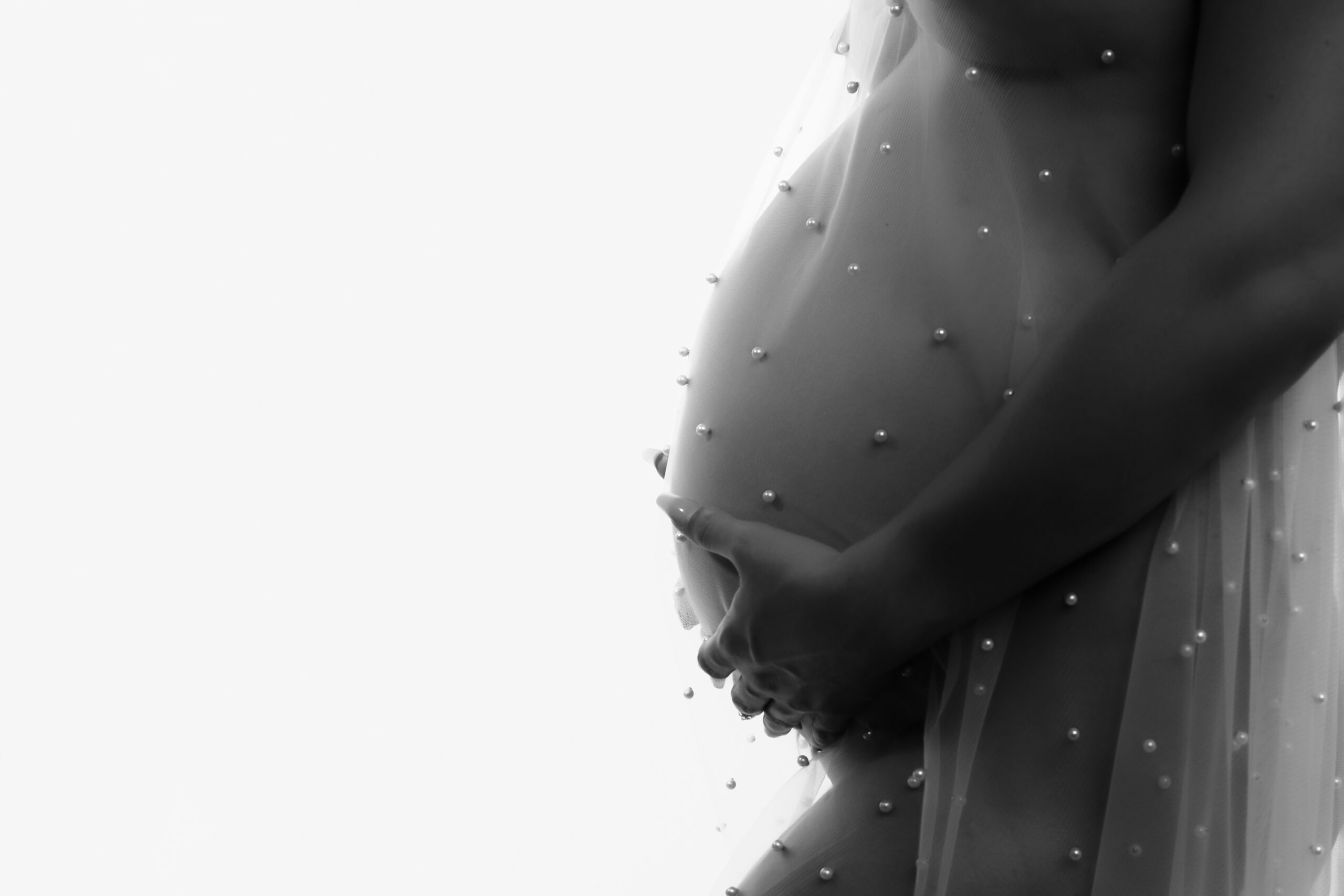 photo of a nude pregnant woman's belly covering her body with a sheer fabric with pearls