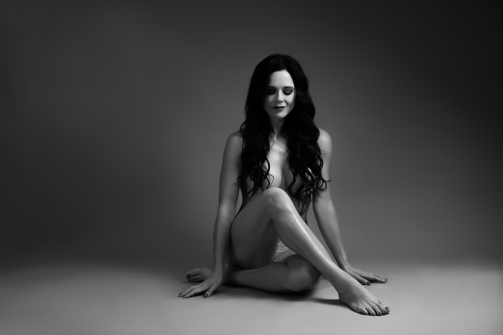 A woman sitting on the floor naked covering her body with her legs and long hair covering her breast.