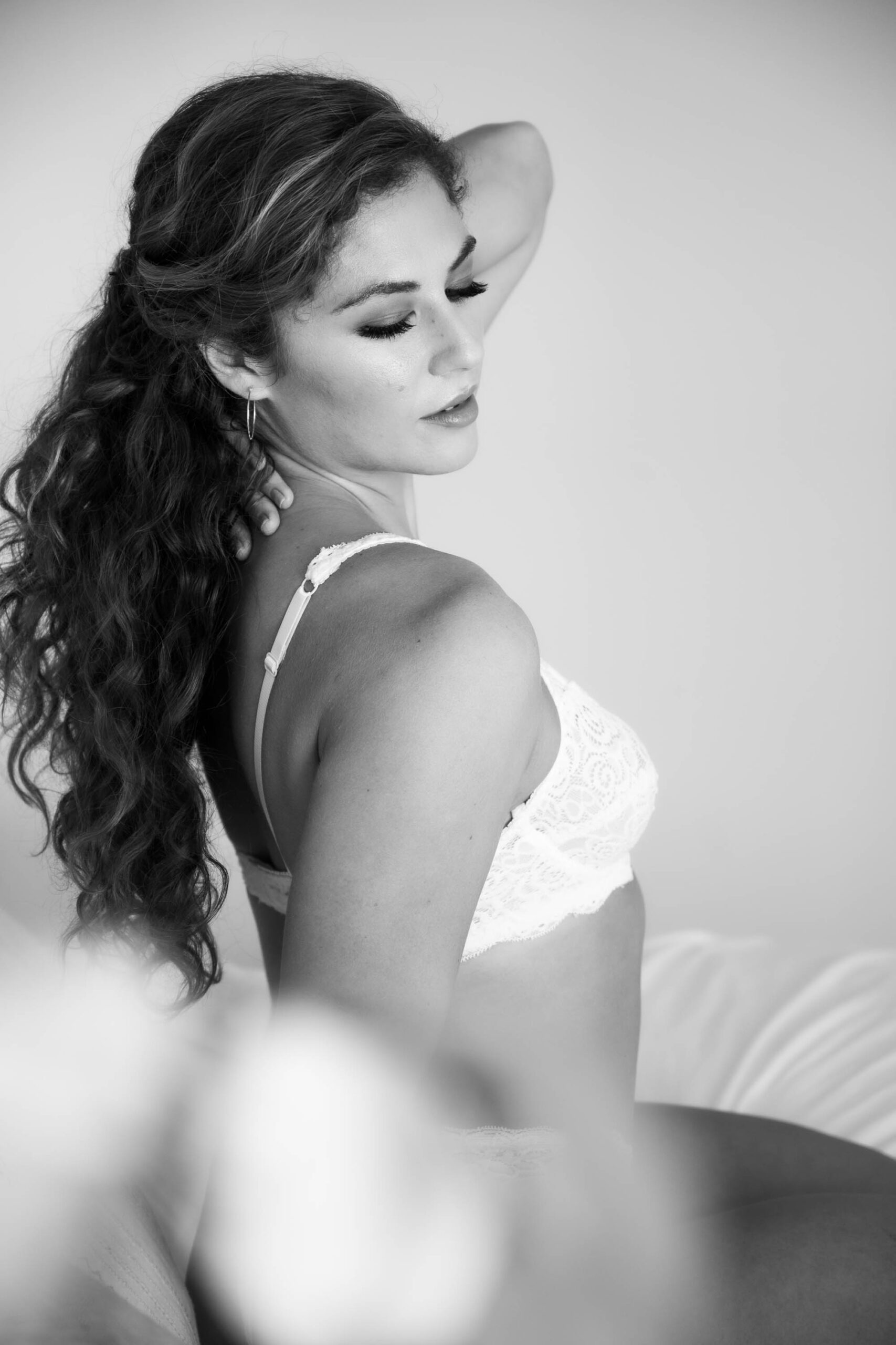 A woman sitting on a bead wearing white lace bra an softly touching her hair