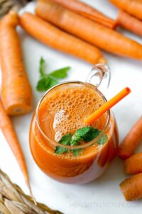 A glass of carrot juice next to fresh carrots