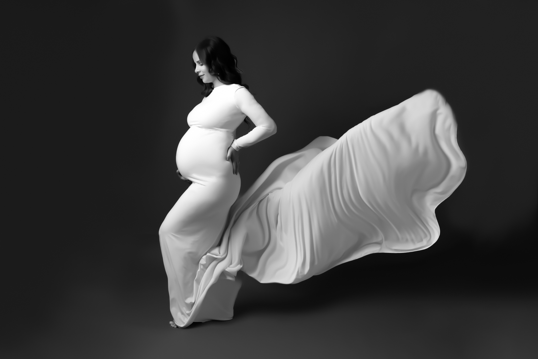 A pregnant woman wearing a white long sleeve dress with a flowy tail