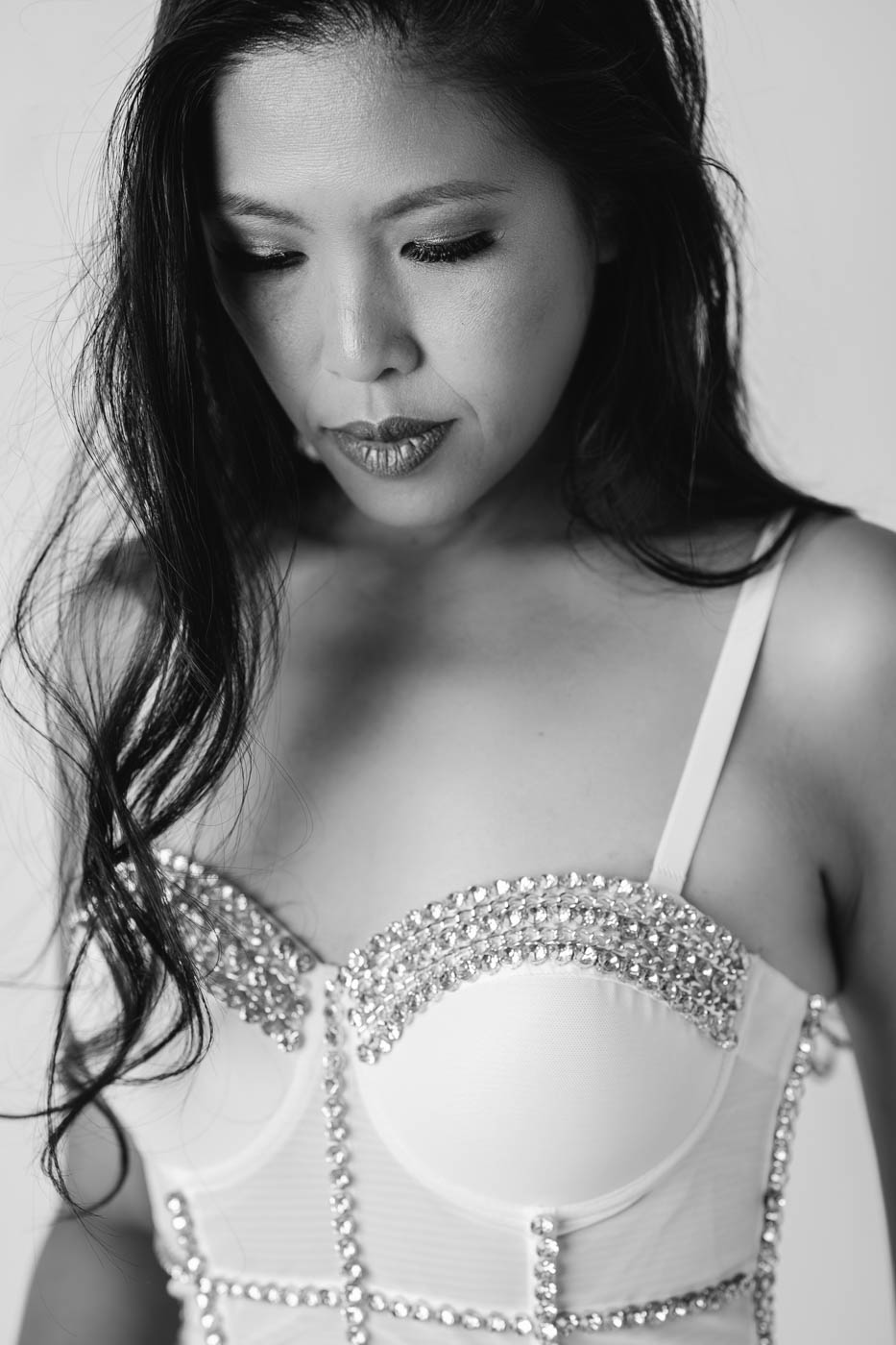 A black and white portrait of a woman wearing a white corset with stones on top