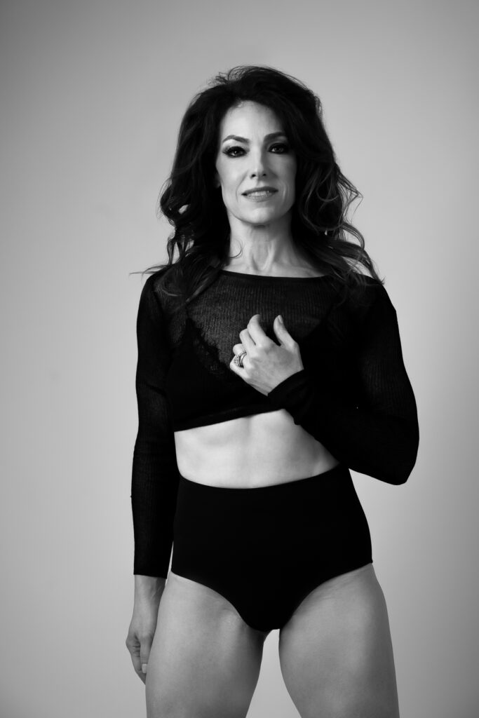 A woman wearing black short shorts and a black top lifting in with one hand showing her abs