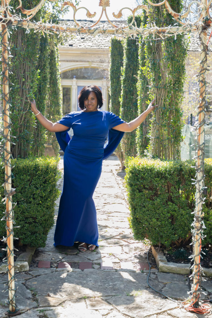 A woman standing in a garden wearing a blue gown