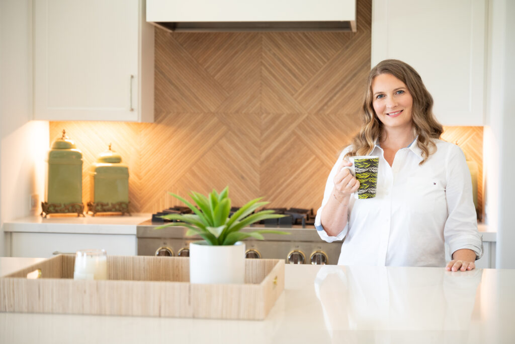 a portrait of a blond woman standing on a kitchen holding a cup of juice