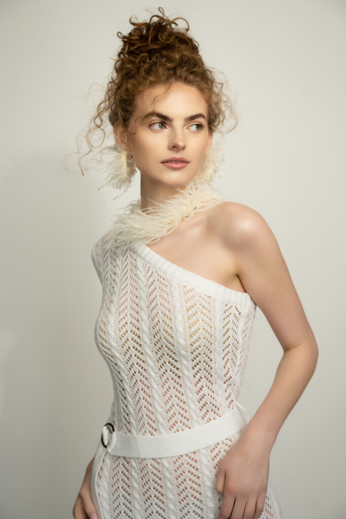 A portrait of a woman wearing a see-through white dress with feathers on the neck