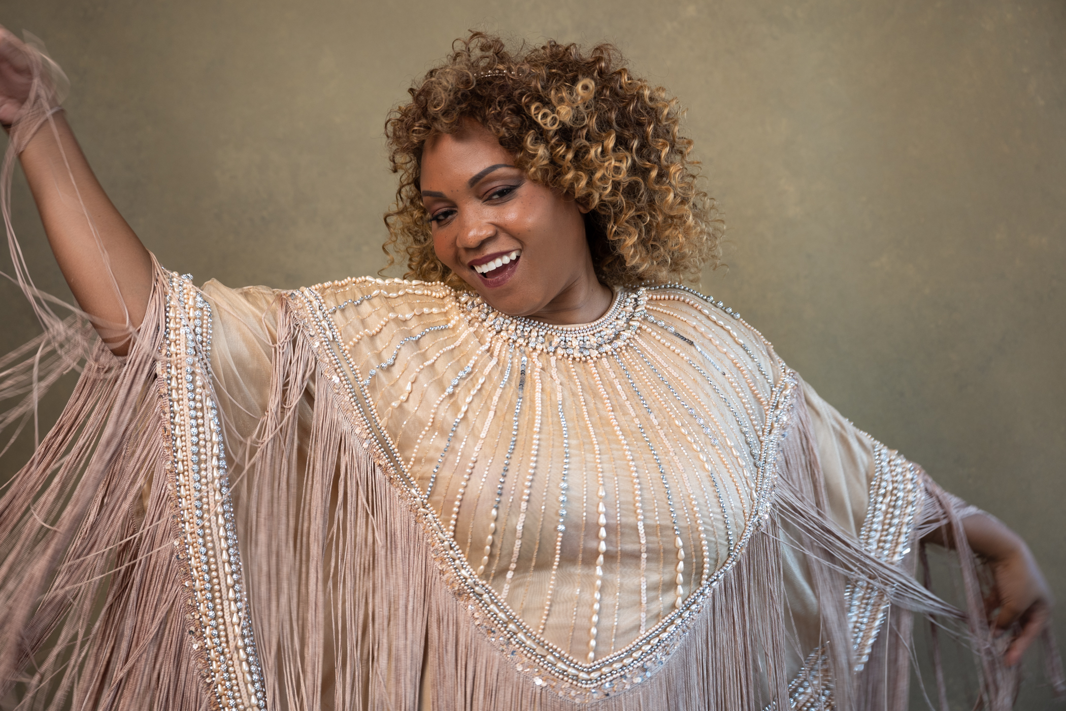 A black woman with short curly hair smiling to the camera wearing a pink dress